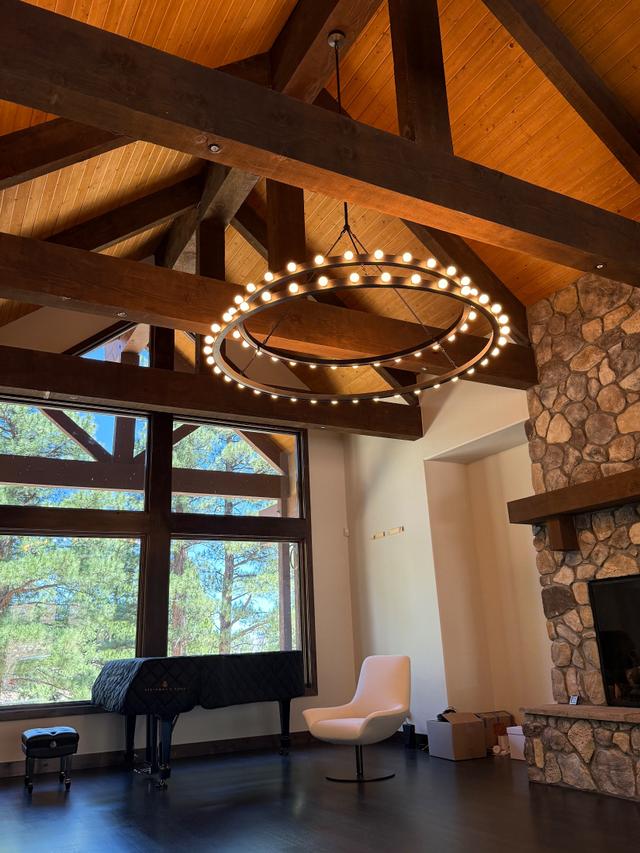 Two-tier ring chandelier hung from dark timber trusses in a vaulted great room