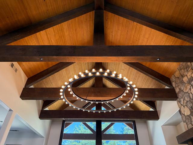 Ring chandelier with dozens of warm bulbs installed under a vaulted beamed ceiling