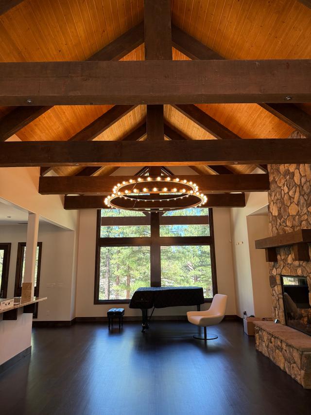 Great room chandelier lighting a grand piano beside a stone fireplace and forest-view windows
