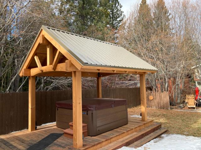 Timber-frame hot tub pavilion with metal gable roof on a backyard deck