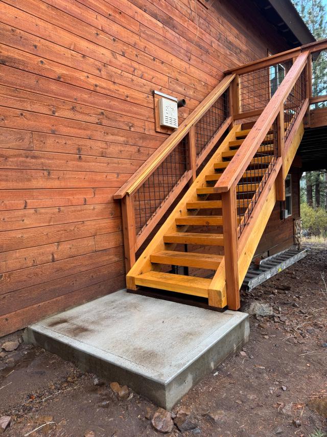 Cedar stairs with hog wire railing panels beside a rustic wood-sided home