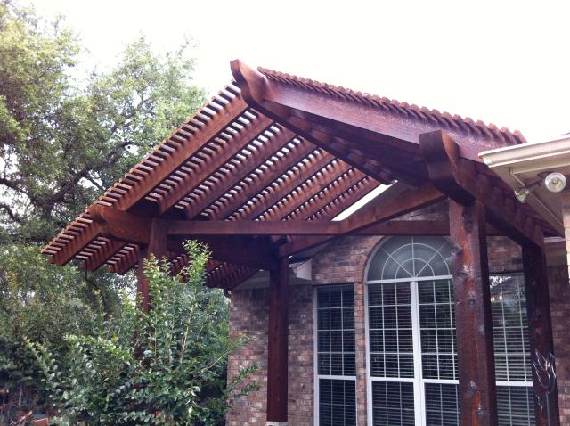 Heavy timber pergola with layered lattice canopy shading a brick home entry