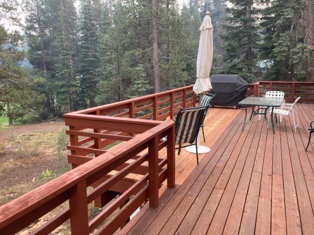 Stained deck with horizontal-board railing, patio dining set, and evergreen forest backdrop