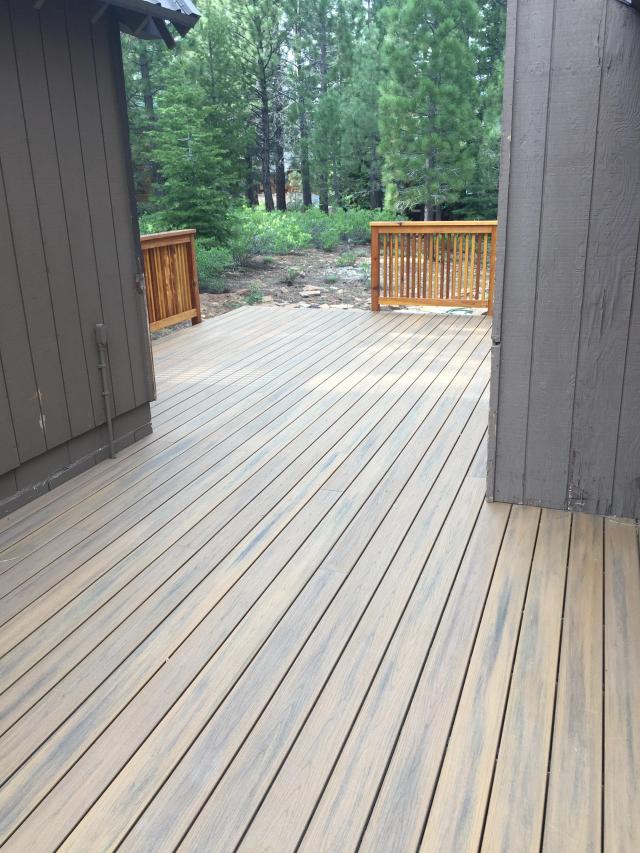 Variegated composite decking with wood railing backed by a pine forest
