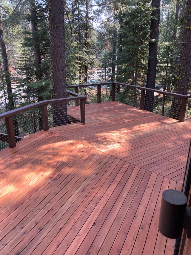 Redwood deck with cable railing and diagonal board inlay beneath tall pines