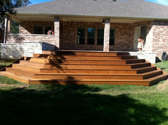 Wide cascading stained-wood steps sweeping down from a brick home's back patio