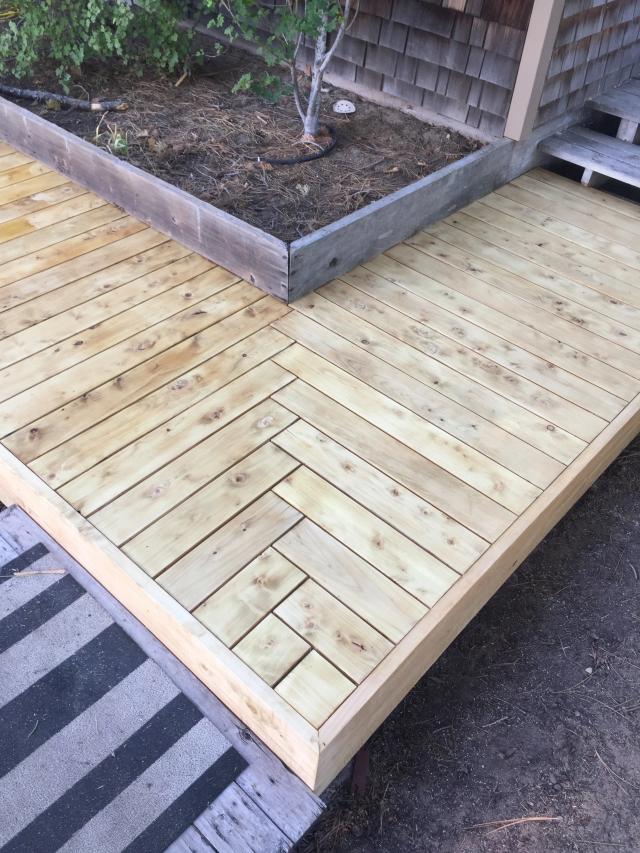 Ground-level cedar platform mixing herringbone and straight decking beside a timber planter
